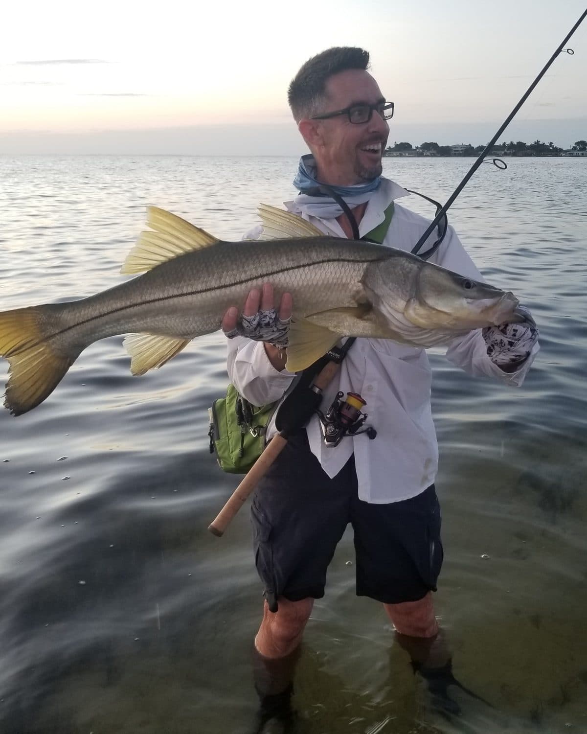 Sean Farro standing in shallow water at dusk, holding a large snook.
